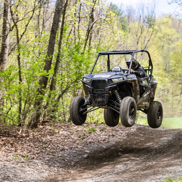 a rzr driving down a dirt road in a forest